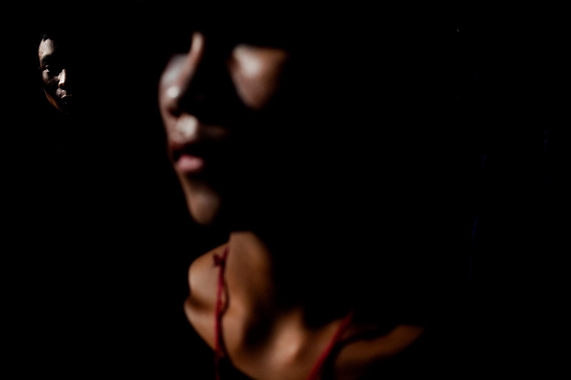 Two faces in near darkness, one catching a sliver of light.