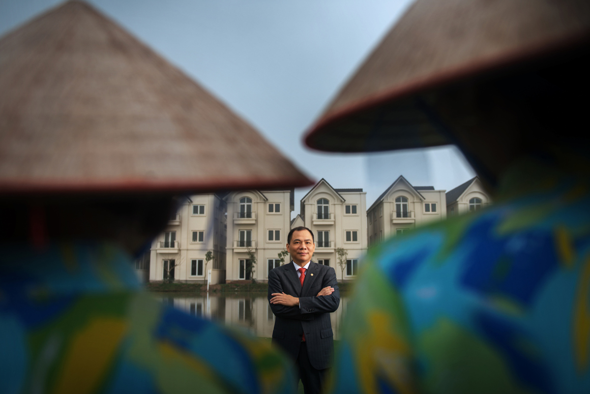 A man in a suit stands before a hotel, framed by two conical hats.