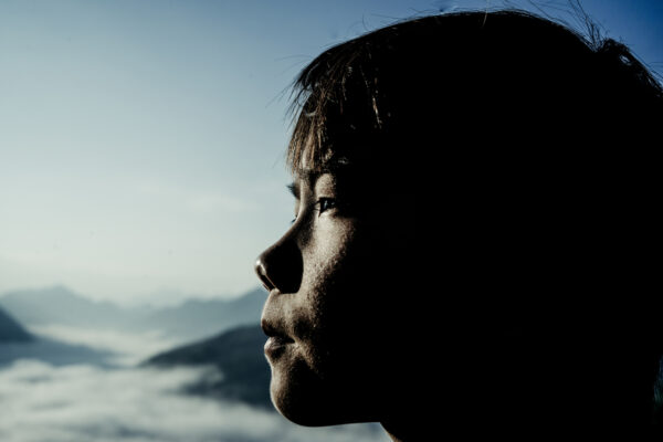Silhouette of a person in profile facing left, overlooking misty mountains and pale blue sky.