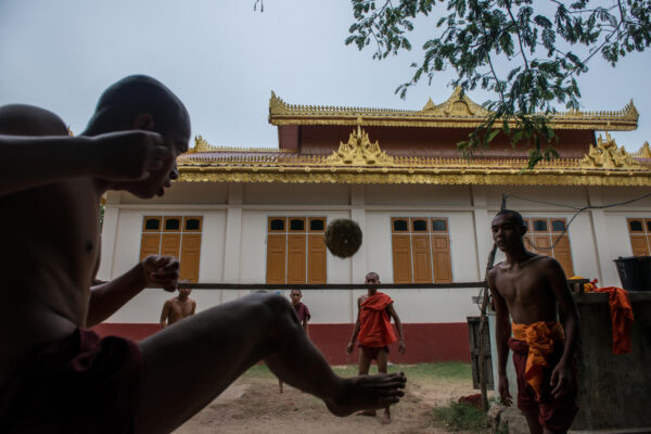 Monks in orange robes playing a ball game in a courtyard with a gold-roofed temple in the background