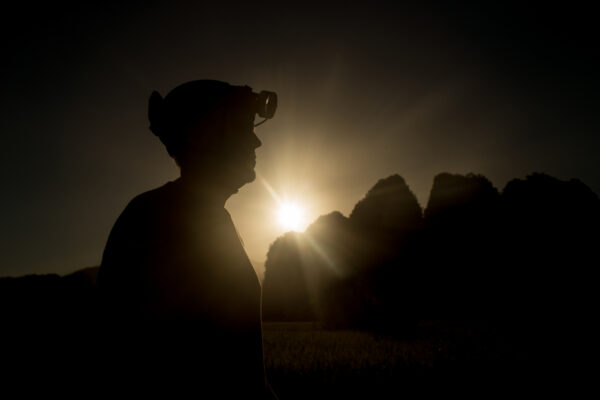 Silhouette of a person wearing a headlamp at sunset, with rugged hills in the background.