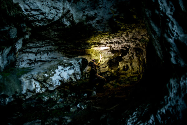 Person kneeling in a dark cave, reaching toward a sunlit rock wall.