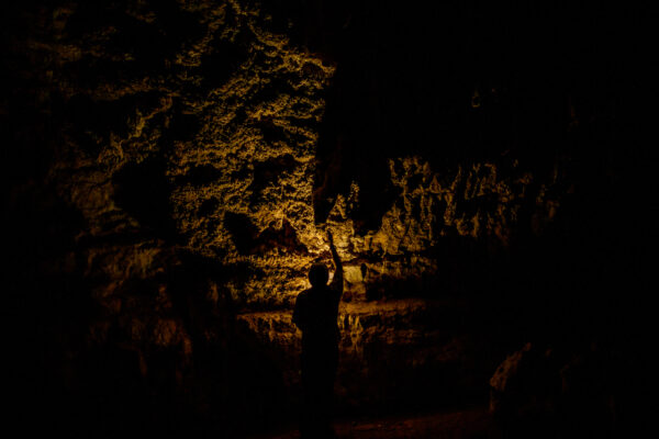 Silhouette of a person in a dark cave, pointing a torch toward illuminated rock walls.