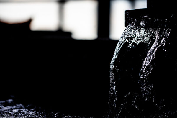 Close-up of water streaming over a dark, curved surface with bright highlights against a black background (high-contrast image).