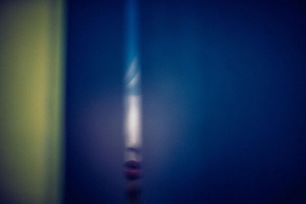 Abstract blurred portrait: partial feminine face with red lips emerging from a blue background with a yellow-green edge on the left.