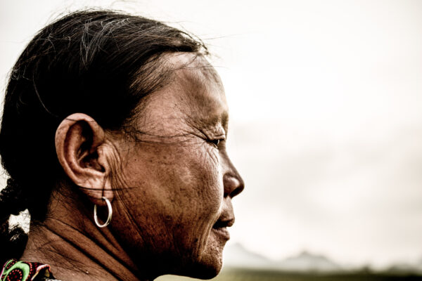 Profile of a woman with a silver hoop earring, facing right, in an outdoor setting with wind in her hair.