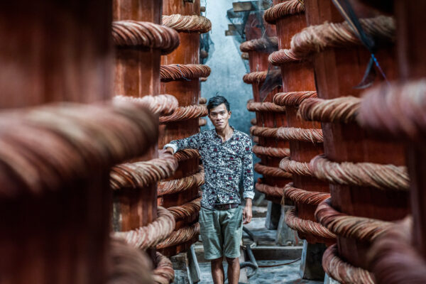 Man standing between two rows of large red wooden posts wrapped with thick ropes, in a narrow industrial alley