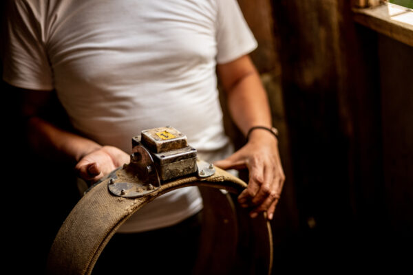 Close-up of a person in a white T-shirt gripping a dusty abrasive wheel mounted on a metal fixture in a workshop.