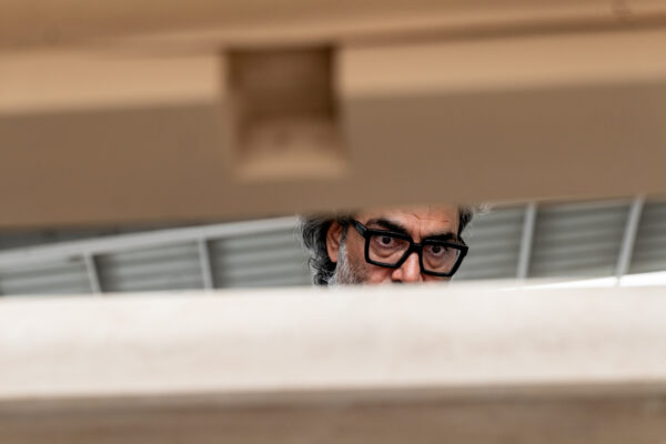 Man with black-framed glasses peeking over a white railing, looking downward