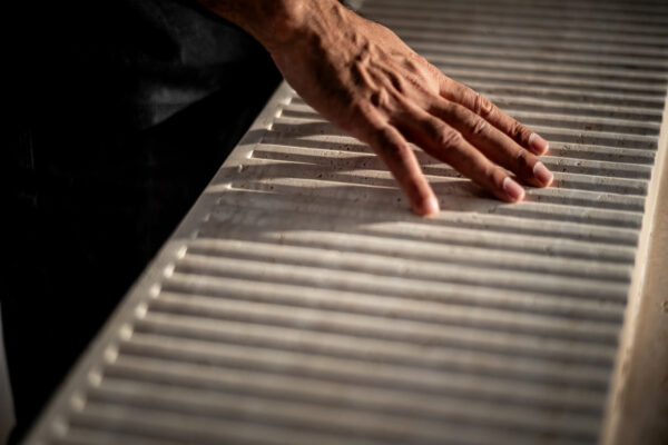 Close-up of a weathered hand with dirt on fingers resting along a ribbed metal surface, like a grill or grate.