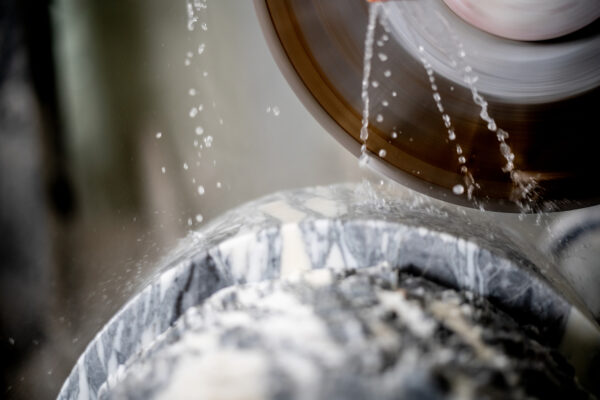 Close-up of a spinning grinding wheel with water spray splashing onto a metal surface, illustrating an industrial grinding process.