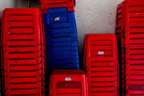 Stacked red and blue plastic chairs stored against a wall indoors.