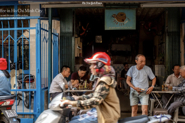 Cafe scene in Ho Chi Minh City with blue storefront gates and locals dining outside, pedestrians and motorbikes in motion.