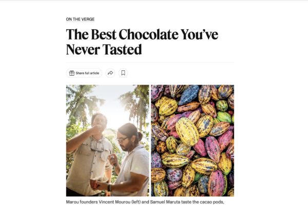 Two men tasting chocolate outdoors beside a grid of brightly colored cacao pods to the right.