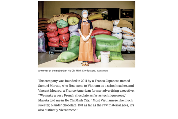 Factory worker wearing an orange apron and mask stands in front of stacked colorful burlap sacks and bags at a warehouse.