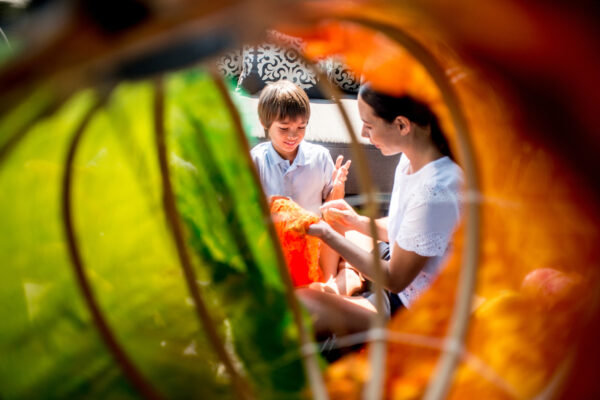 Woman and boy sit inside a brightly colored lantern, focused on an orange crafts project.
