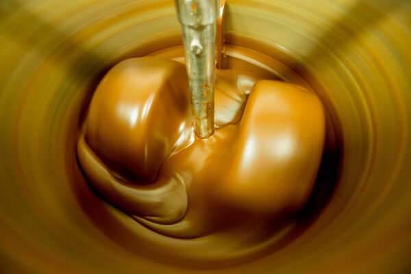 Close-up of a metal mixer stirring melted chocolate in a spinning vat.