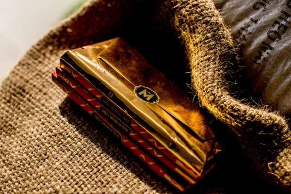 Stack of four small cigar boxes with red patterned sides, labeled 'Single Origin Vietnam', resting on coarse burlap fabric.