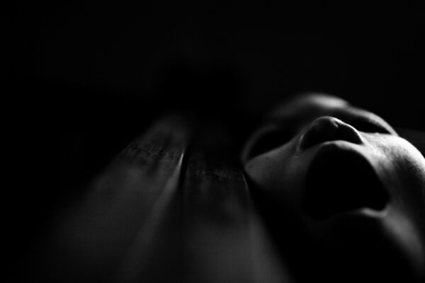 Close-up of a person's face in deep shadow, only the nose and lips subtly illuminated.