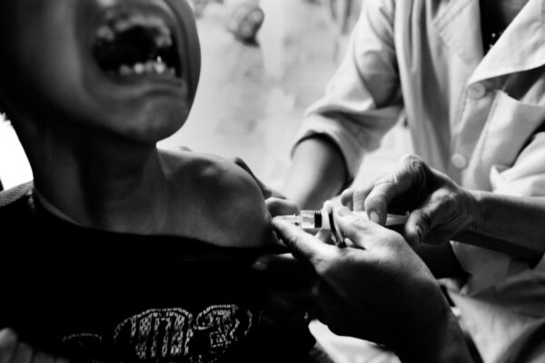 Medical professional administering a vaccine to a patient's shoulder in a close-up, black-and-white photo.