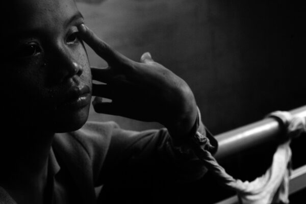 Close-up black-and-white portrait of a person resting their temple on their fingers, looking thoughtful or somber.