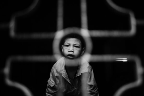 Boy peering through a circular hoop on a playground, looking at the camera in a black-and-white shot.