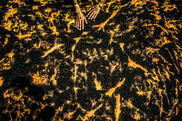 Close-up of two hands resting on a dark, orange-and-black textured surface with a rough, patterned pattern (rusty or volcanic-looking).