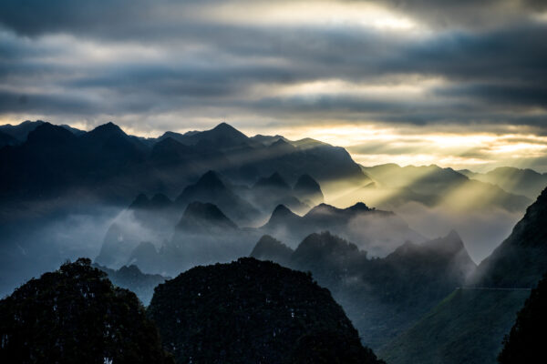Misty mountain range at dawn with sunbeams breaking through clouds over dark peaks