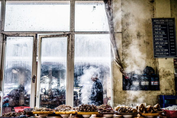 Shellfish displayed in bowls along a counter inside a dusty market stall, with a foggy window and a menu board on the wall behind.